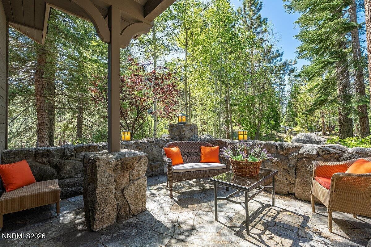 Stone patio at 1 Kelly Cir with orange-cushioned seating, granite boulder walls, lanterns hung on the boulders, and a clearing of pines opening behind