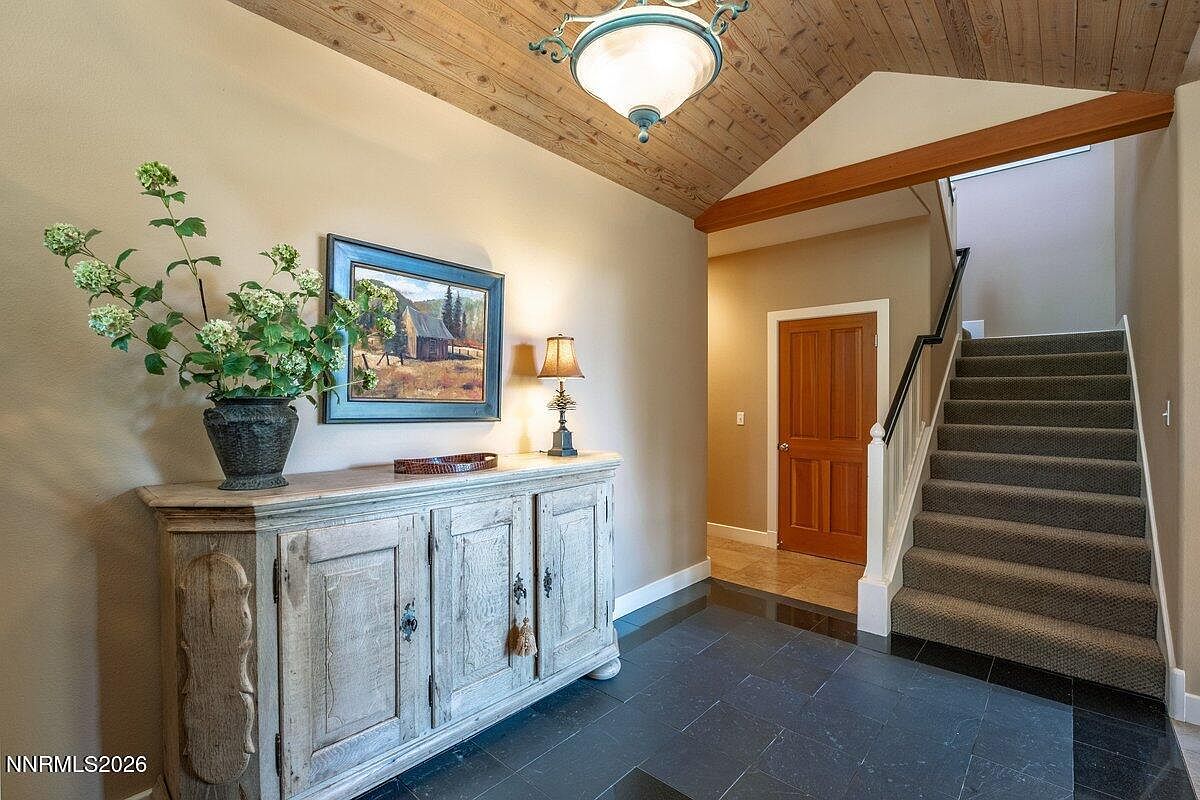 Foyer of 1 Kelly Cir with vaulted tongue-and-groove wood ceiling, slate floor, antique sideboard with hydrangeas, and a carpeted stair rising to the second level